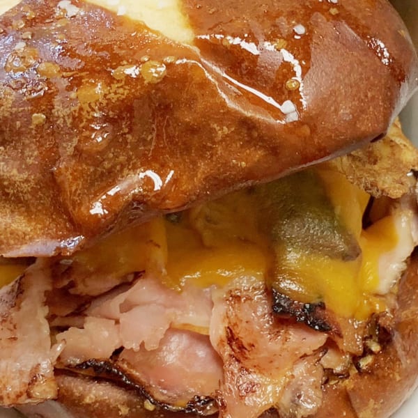 Close-up of a MadMacs sandwich with melted cheese, ham, and a pretzel bun.