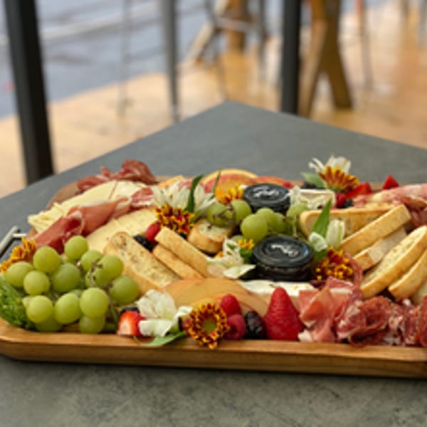 A large charcuterie board with cheeses, meats, grapes, berries, bread, and flowers on a table.