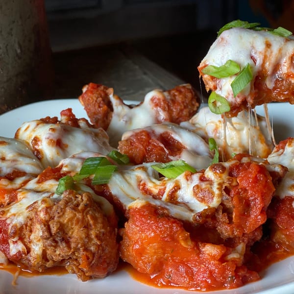 Cheesy MadMacs meatballs with marinara sauce and green onions, one being lifted with cheese pull.