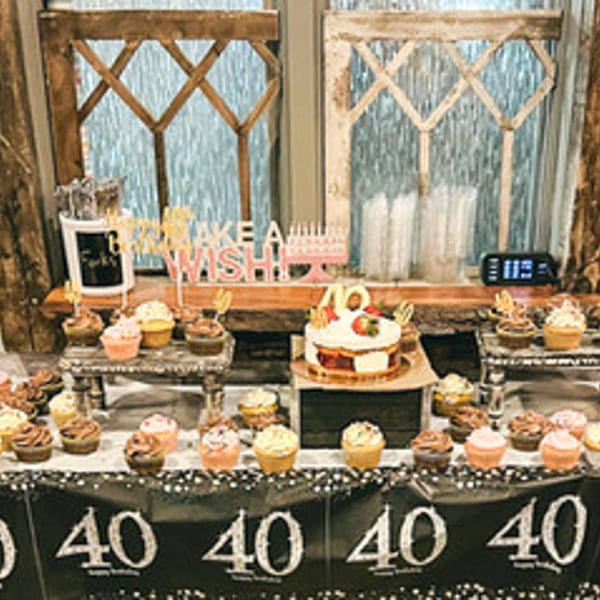 A dessert table with a cake, cupcakes, and "Make a Wish" and "40" decorations.