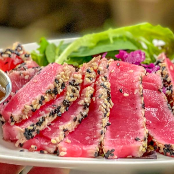 Seared tuna slices with sesame seeds, served with a side of green and purple salad.