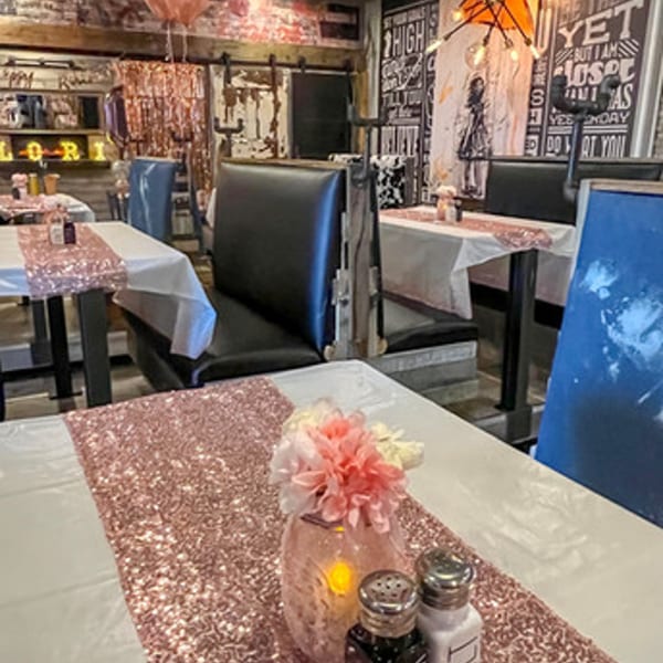 A MadMacs dining area with tables set with white tablecloths, rose gold sequin runners, and floral centerpieces.