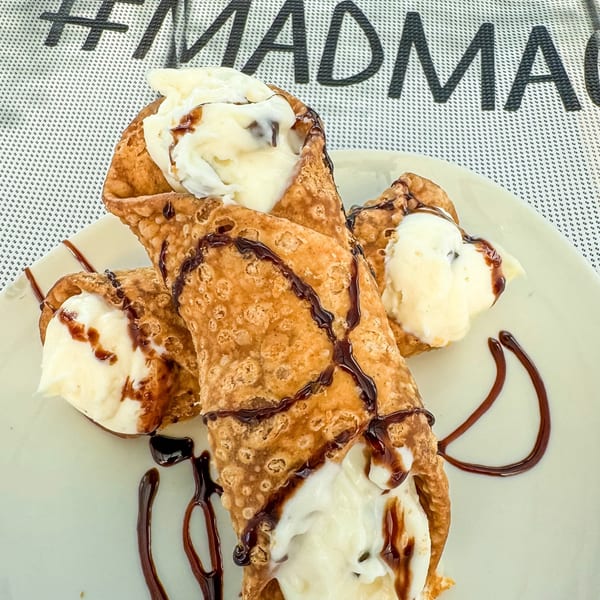 Three MadMacs cannolis filled with white cream and drizzled with chocolate sauce on a white plate.